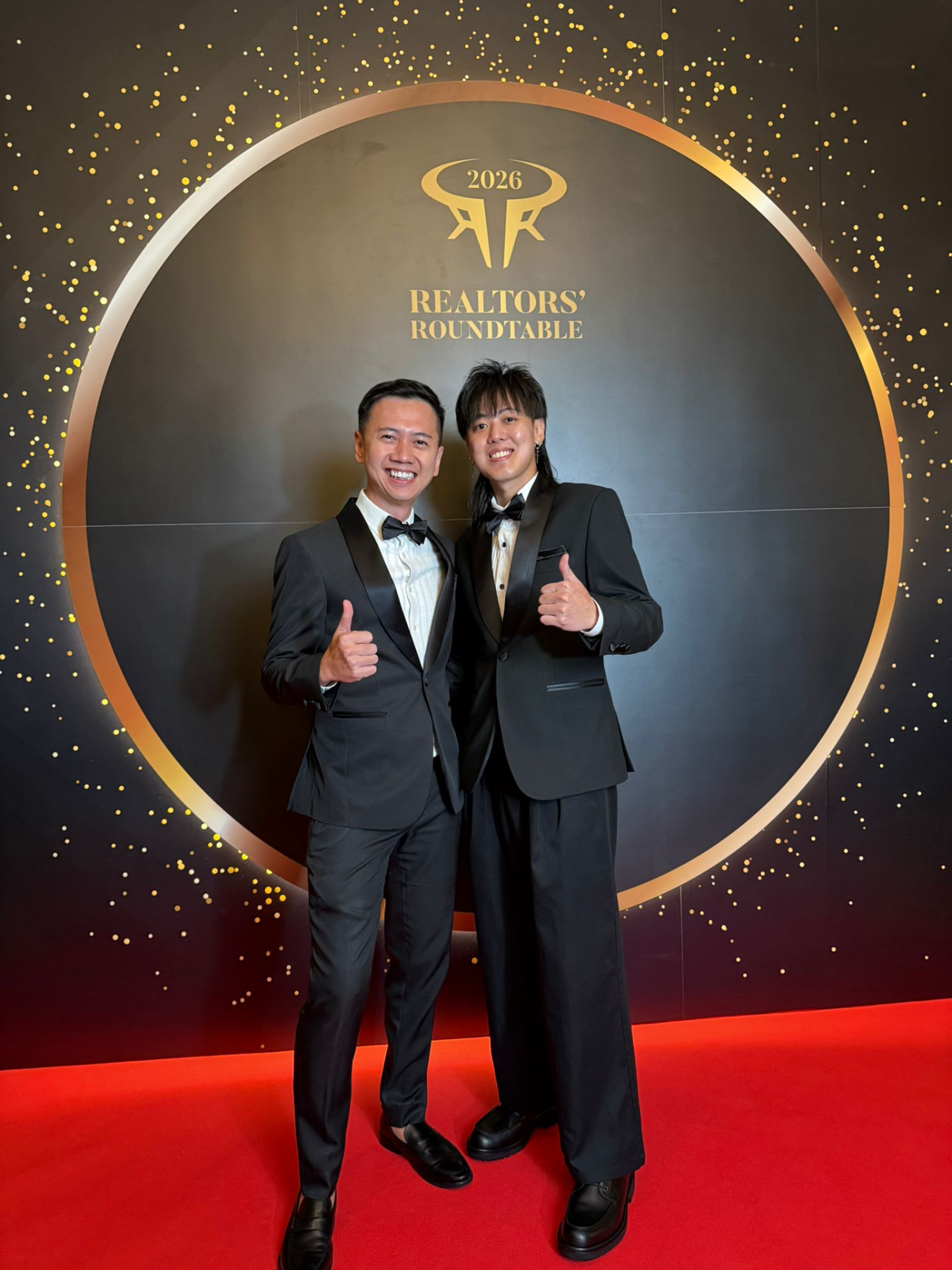 Fendy Lee with a colleague in tuxedos at the 2026 Realtors' Roundtable, giving a thumbs up on a red carpet